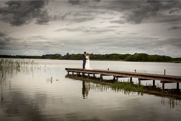 A bride and groom standing on a dock near a lake, captured by their wedding photographer.