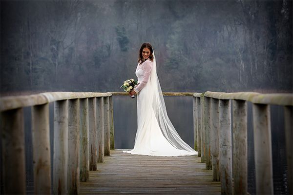 A bride standing on a wooden bridge near a lake, captured by a wedding photographer.